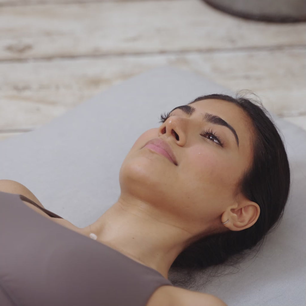 A video of a woman peacefully lying in Shavasana on a Maya Shanti Yoga mat wearing an MSY Lavender Eye Pillow - Hemp, Lavender & Linseed, engaged in meditation.